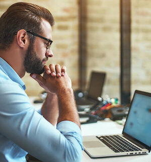 Nachdenklicher Mann am Schreibtisch blickt konzentriert auf Laptopbildschirm